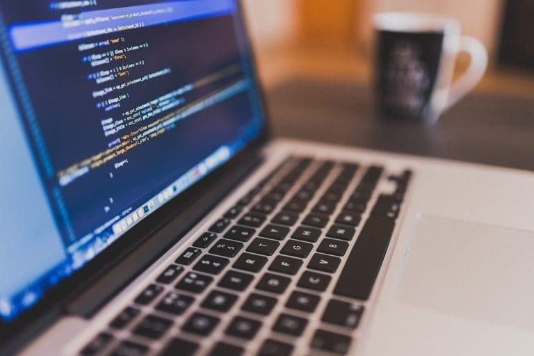 ein aufgeklapptes Macbook mit Coding-Zeilen und einer Kaffeetasse im Hintergrund