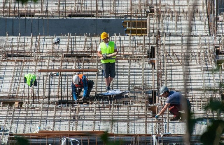 3 Bauarbeiter mit Warnkleidung auf einer Baustelle in einem Rohbau mit Drahtgeflechten